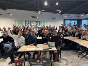 Groep mensen viert enthousiast in moderne kantoorruimte van The Greenbox met opgestoken handen en glimlachen