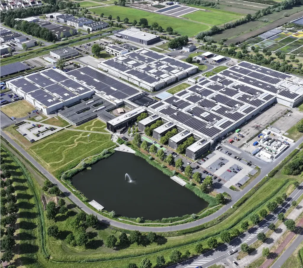 Luchtfoto van industriële campus met zonnepanelen op daken, omgeven door logo's van duurzame energie bedrijven