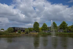 Modern gebouw aan meer met fontein, omgeven door groene bomen onder bewolkte hemel