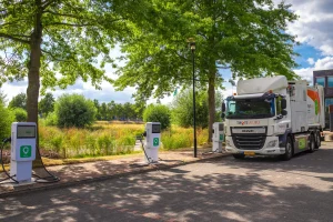 DAF vrachtwagen van Twente Milieu wordt opgeladen bij groene laadpalen in een park met bomen en groen landschap op de achtergrond.