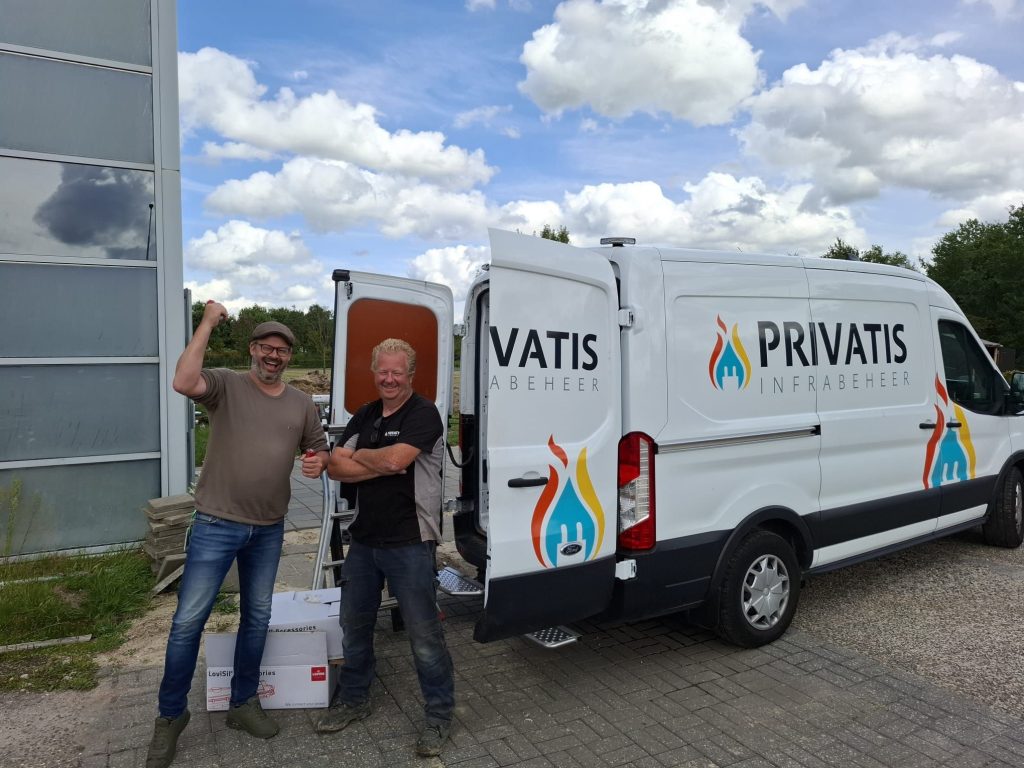Twee mannen poseren bij een witte bestelwagen van Privatis Infrabeheer met open achterdeuren op een bedrijfsterrein.