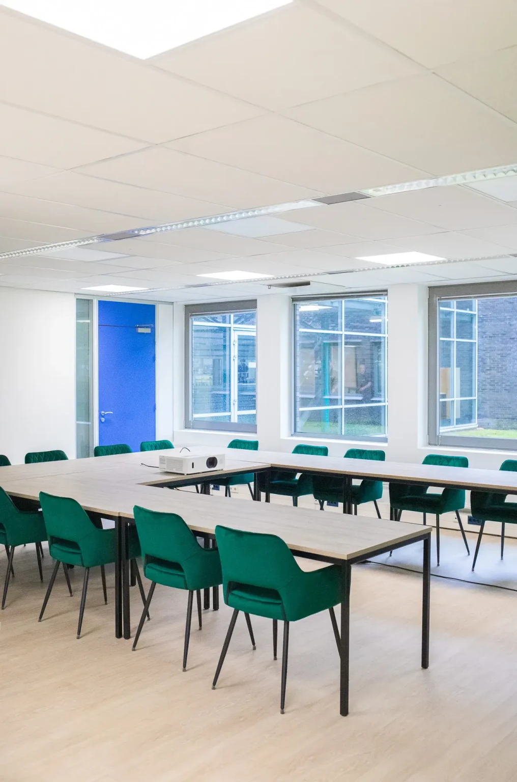 Moderne vergaderruimte met groene stoelen, witte tafels en grote ramen in kantoorgebouw