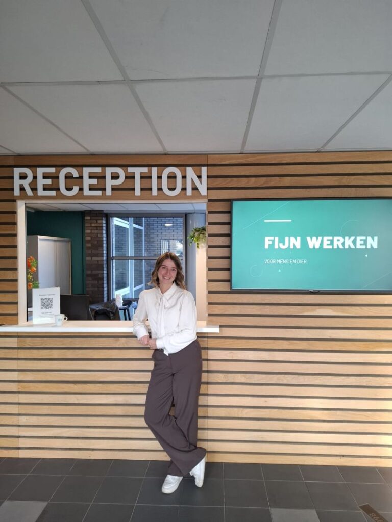 Vriendelijke receptioniste bij moderne houten receptiebalie met FIJN WERKEN display in professionele kantooromgeving