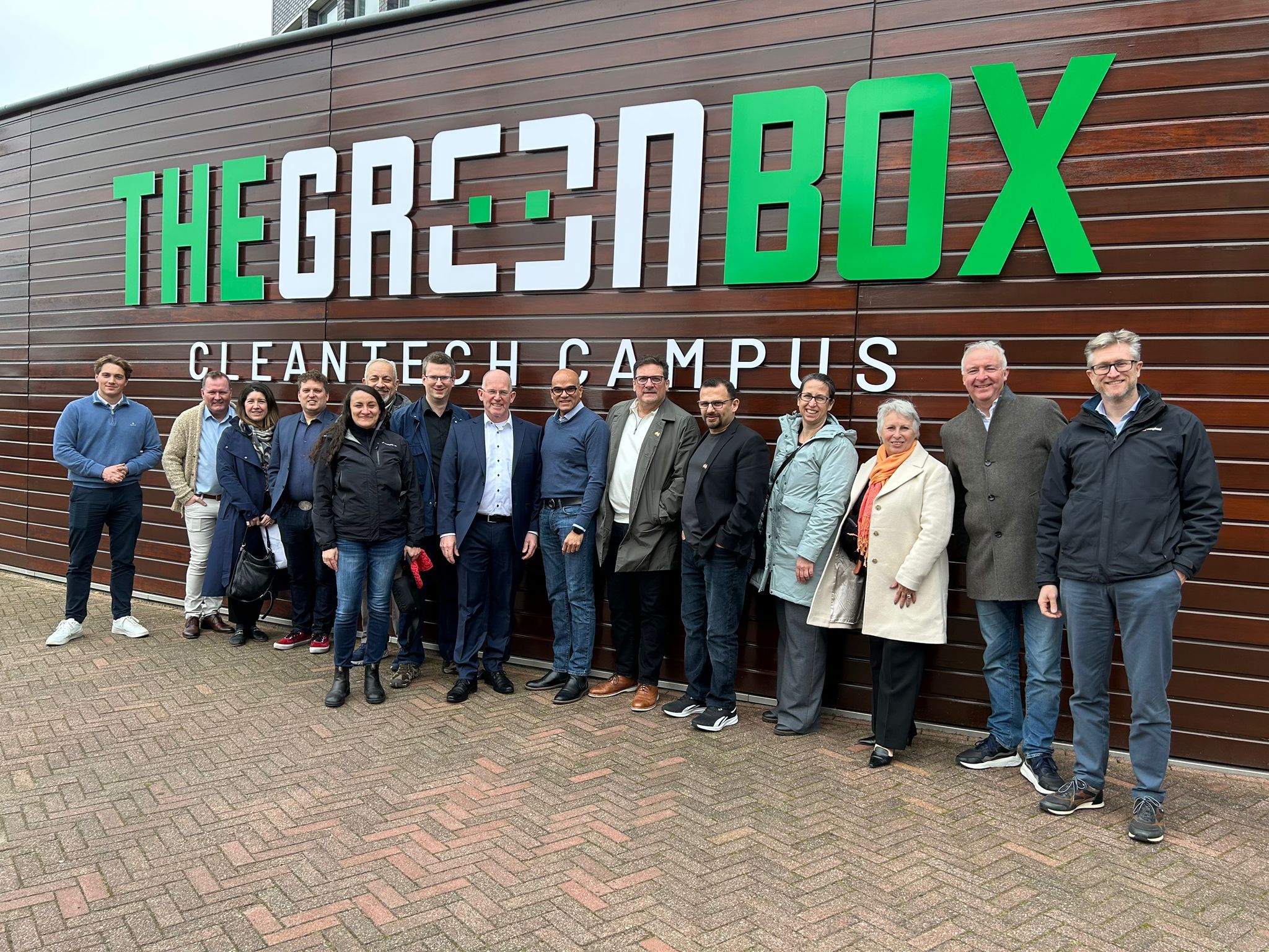 Groep mensen poseert voor het bord van The Green Box Cleantech Campus, een duurzame technologie innovatiehub.