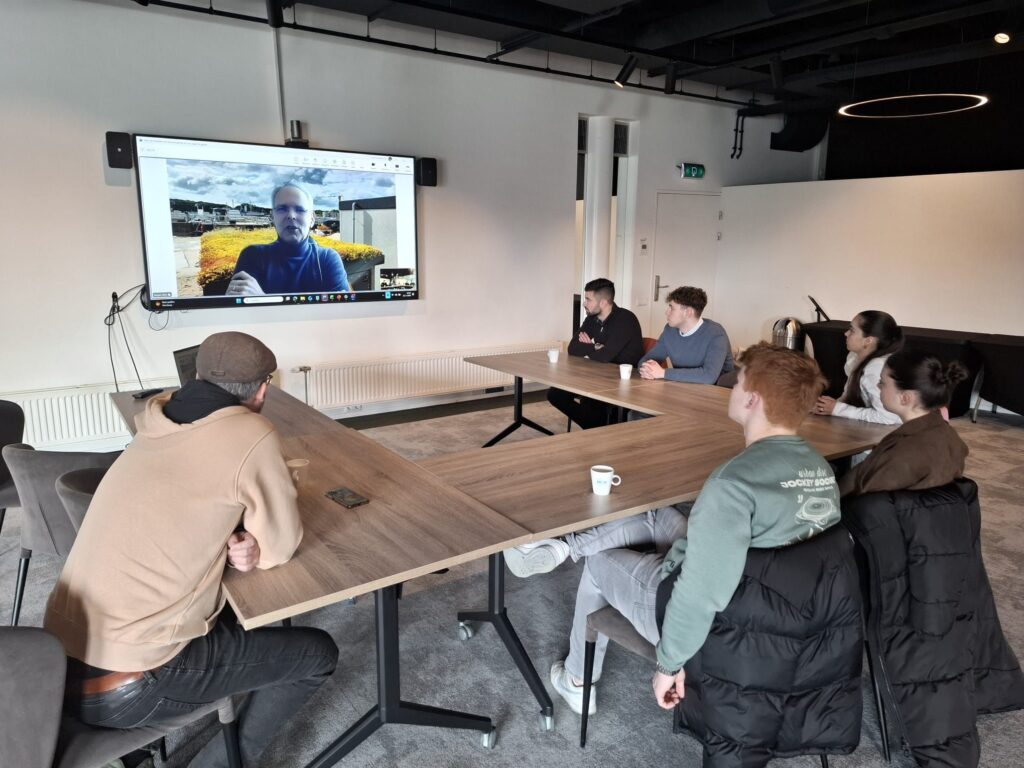Team meeting in modern conference room with video call participant displayed on wall-mounted screen