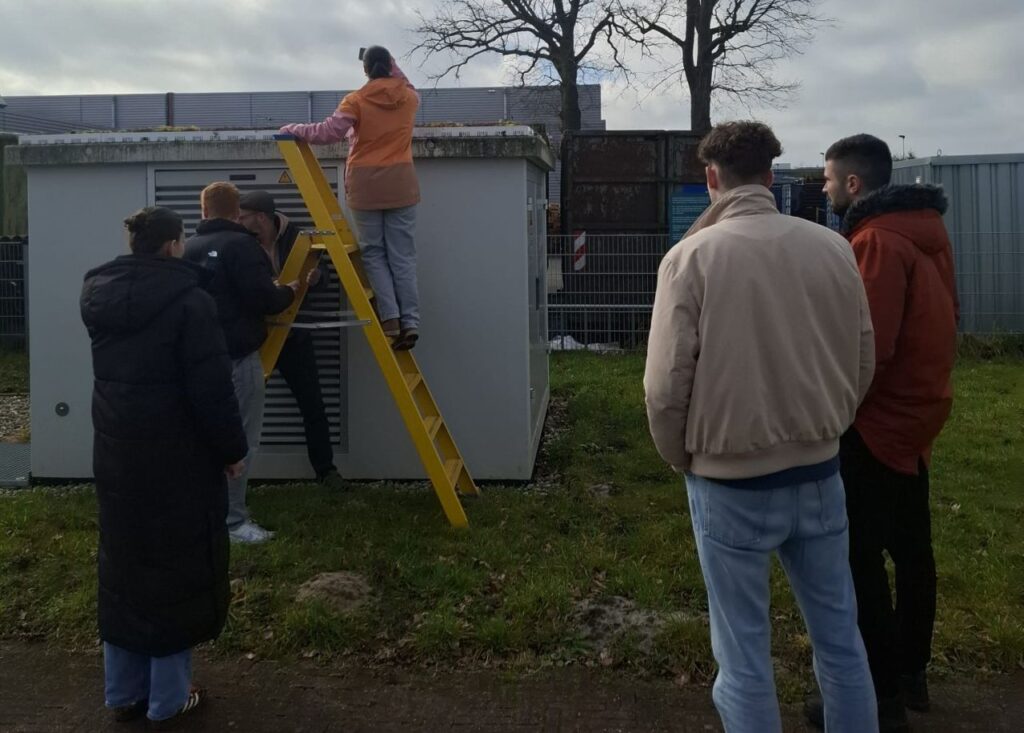 Groep mensen bij HVAC-unit met gele ladder, één persoon klimt omhoog voor onderhoud of installatie op grasveld