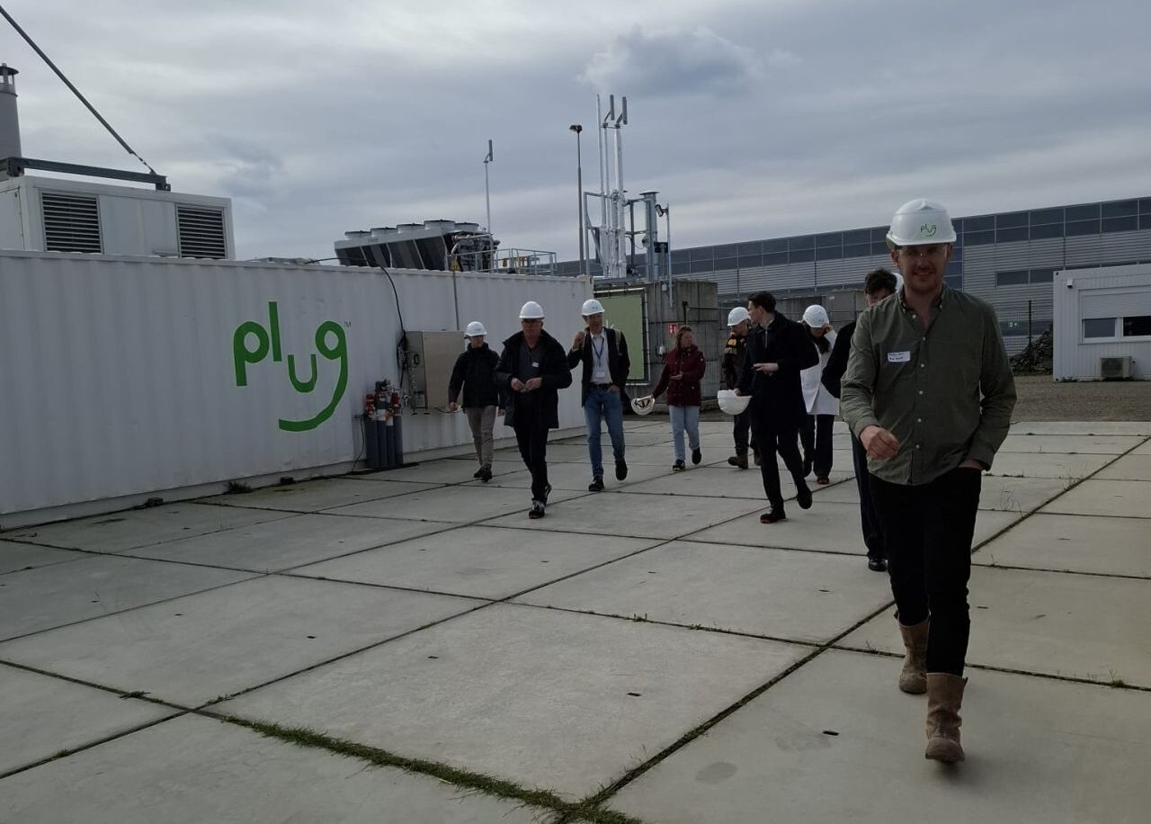 Groep mensen met witte helmen op industriële site tijdens bedrijfsrondleiding bij Plug Power waterstoffaciliteit