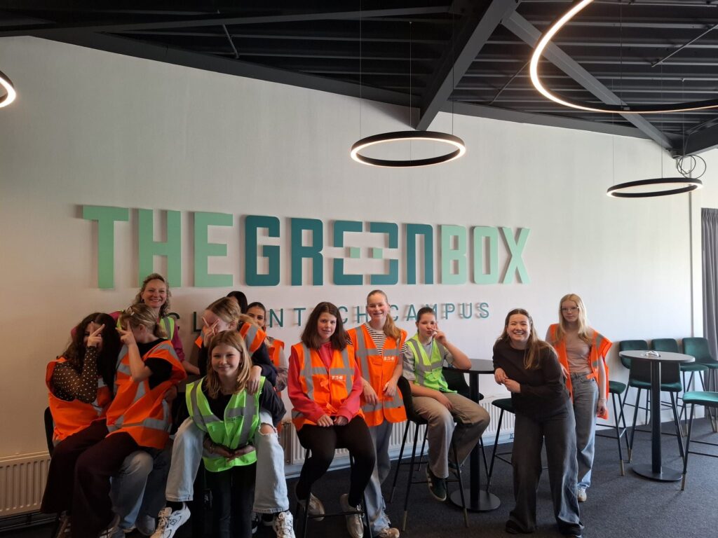 Groep studenten in veiligheidsvesten poseert voor The Greenbox logo op Fontys Tech Campus tijdens bedrijfsbezoek