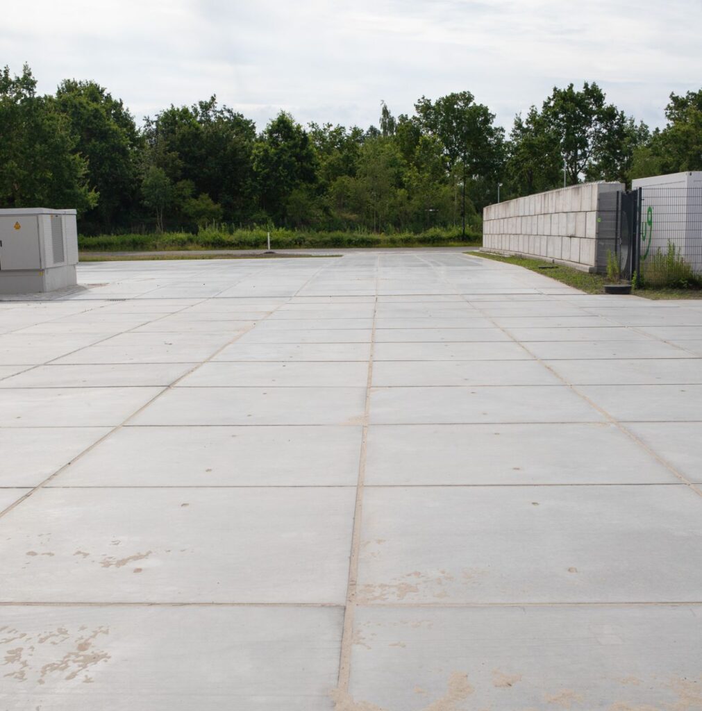 Lege betonnen buitenopslag met betonnen platen, omheining en groen op de achtergrond.