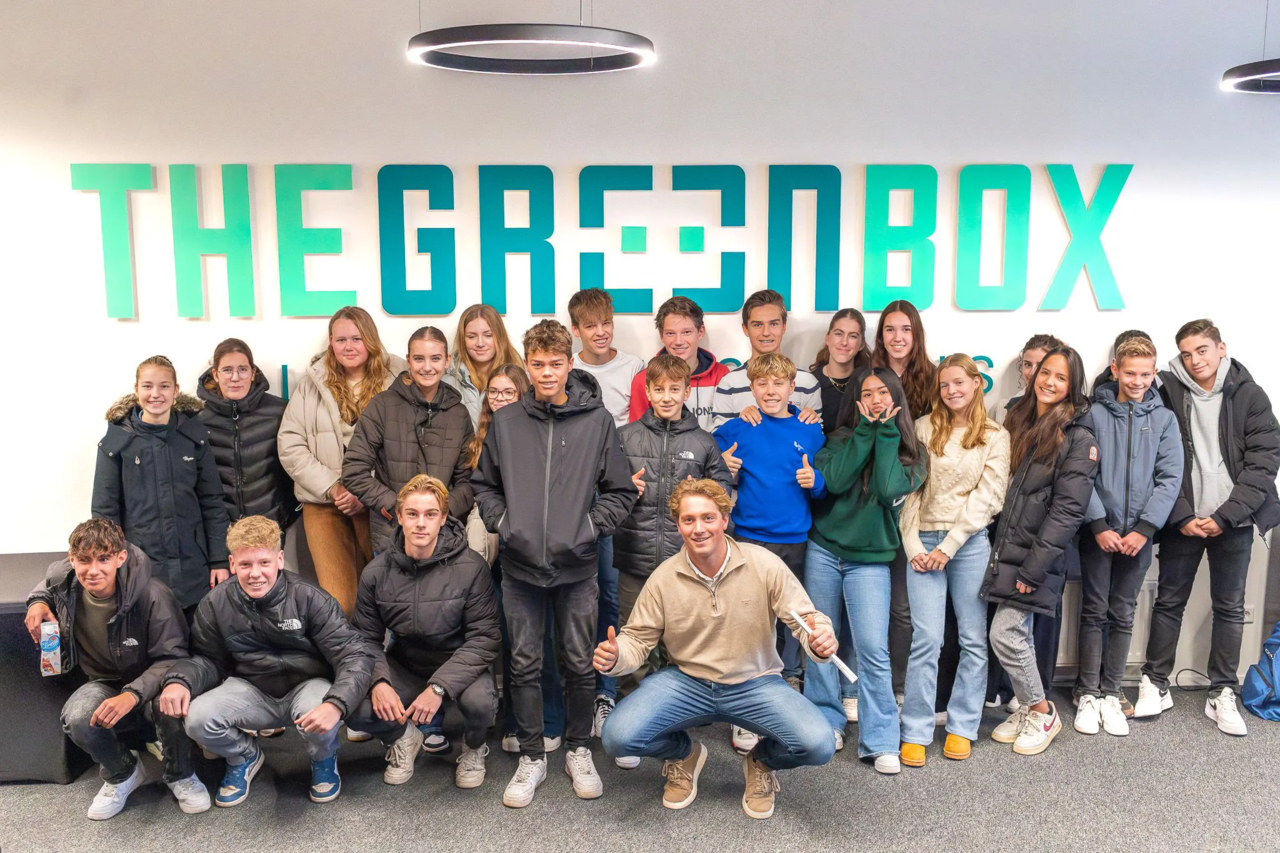 Groep jongeren poseert voor The Green Box logo tijdens een bedrijfsbezoek met begeleider.